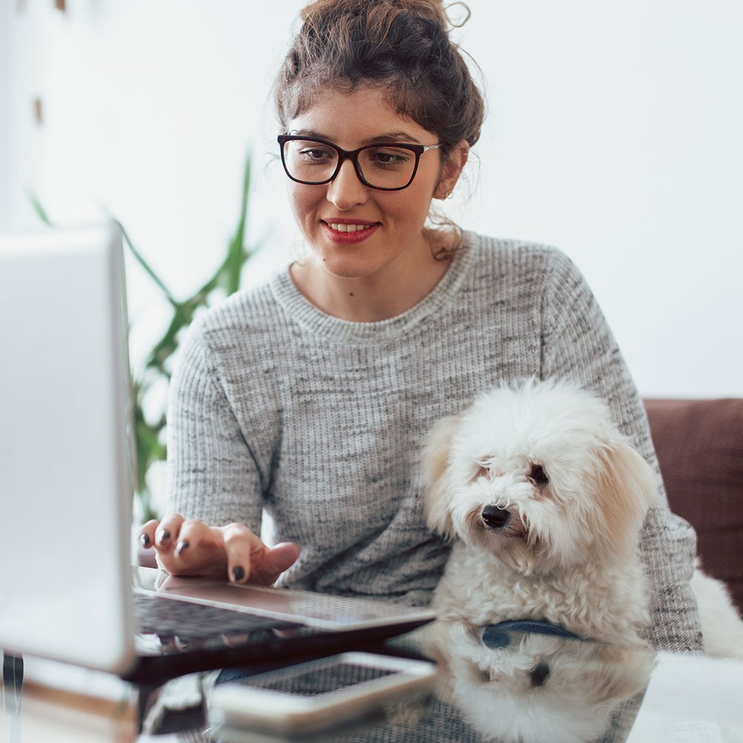 a woman with her small white dog looking at payment options on her laptop